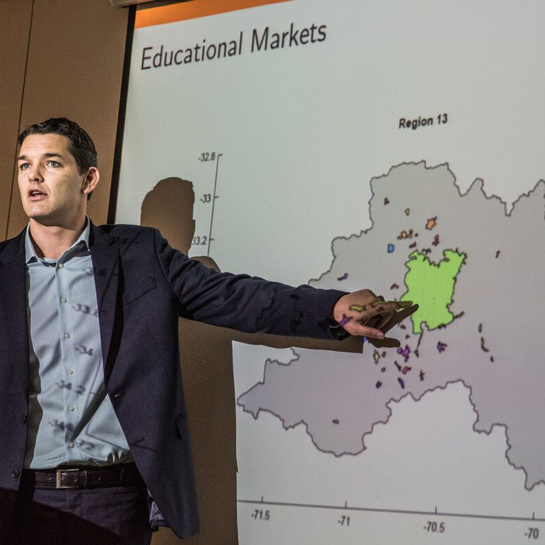 Professor Neilson presenting educational markets research and pointing to a map of schools